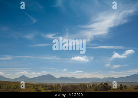 Wispy nuvole sopra un lontano African mountain range con una frizione di alberi Foto Stock