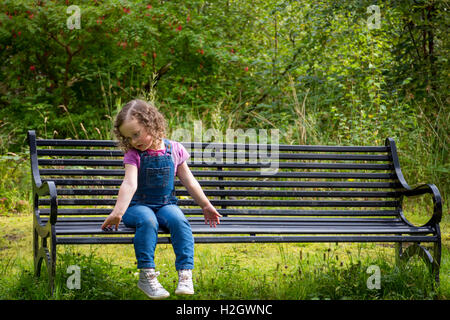 Piccola ragazza seduta su una panchina nel parco Foto Stock