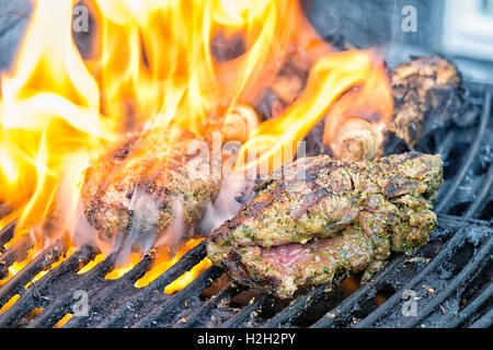 Bistecche marinate al barbecue, fiamme provenienti dal fat che sgocciola la carne nella griglia. Foto Stock