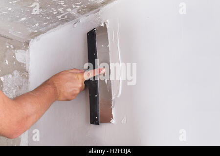 Miglioramento della casa da lavoratore mette lo strato di finitura di stucco sulla parete utilizzando una spatola di intonacatura Foto Stock