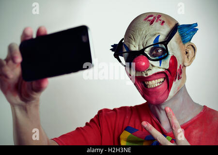 Ritratto di un male spaventoso clown prendendo un selfie con il suo smartphone, mentre dando un segno V Foto Stock