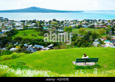 Lone donna seduta sul banco di lavoro e guardando all'oceano dalla sommità del monte Eden Foto Stock
