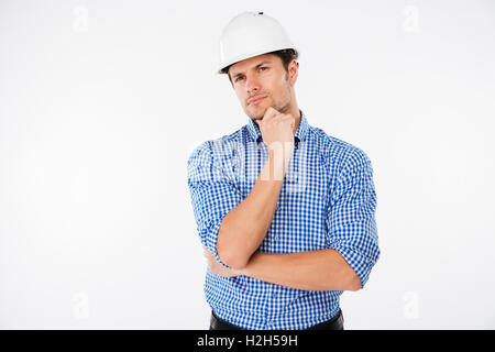 Pensieroso giovane builder in hard hat standng e pensare Foto Stock