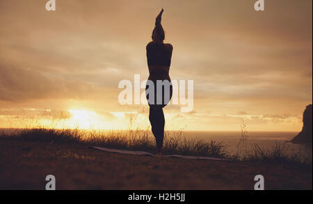Silhouette di una donna che pratica yoga, Garudasana, posa dell'aquila. fitness donna in piedi sul tappetino facendo yoga con braccia e gambe Foto Stock