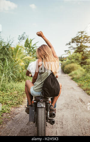 Vista posteriore del colpo di coppia giovane godendo di giro in moto su strada sterrata. Donna seduta su torna con il suo braccio sollevato. Foto Stock