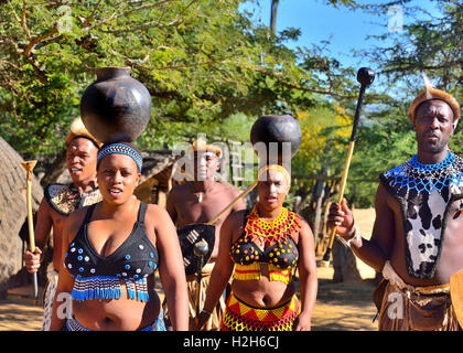 La troupe di Zulu con girl performers che trasportano le bocce d'acqua durante uno spettacolo Zulu Experience al Villaggio Culturale di Shakaland, Eshowe, Sud Africa Foto Stock