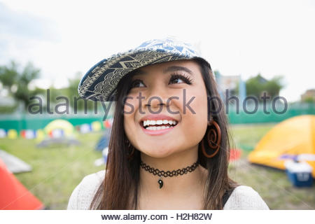 Ritratto di giovane sorridente brunette donna con berretto da baseball guardando il festival musicale estivo Campeggio