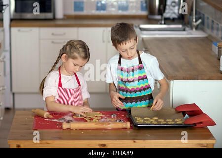 Ragazzo e una ragazza forme di taglio di un collegamento per la pasticceria biscotti in cucina Foto Stock