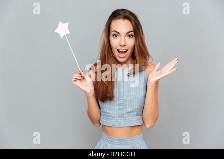 Sorpreso eccitato giovane donna con la bacchetta magica su sfondo grigio Foto Stock