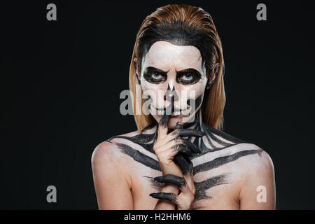 Donna con paura Halloween trucco che mostra il silenzio gesto su sfondo nero Foto Stock