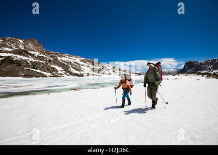 Una giovane donna e uomo escursionismo sulla neve passato un lago ghiacciato in Wind River montagne del Wyoming, STATI UNITI D'AMERICA