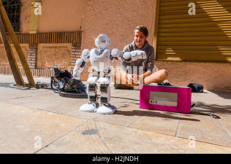 Una ventina di qualcosa di maschio si siede sul marciapiede con il suo robot di eseguire per passanti come egli tenta di panhandle per denaro. Foto Stock