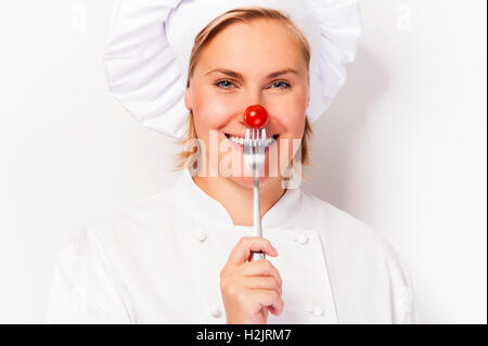 Lo chef donna holdinh una forcella con pomodoro contro il suo naso, in piedi contro uno sfondo bianco sorridente. Foto Stock