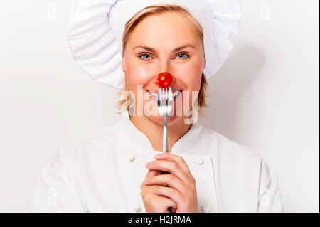 Lo chef donna holdinh una forcella con pomodoro contro il suo naso, in piedi contro uno sfondo bianco sorridente. Foto Stock