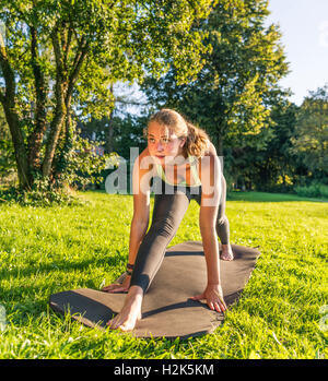 Spacchi frontali, giovane donna in abbigliamento sportivo facendo allenamento sul tappeto nel parco, Monaco di Baviera, Baviera, Baviera, Germania Foto Stock