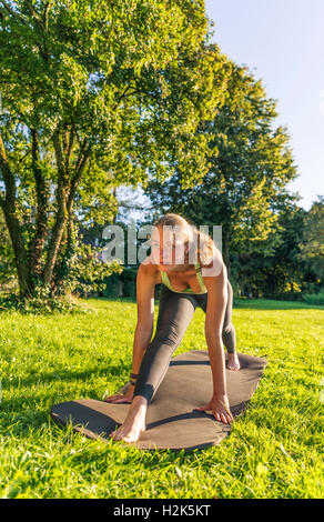 Spacchi frontali, giovane donna in abbigliamento sportivo facendo allenamento sul tappeto nel parco, Monaco di Baviera, Baviera, Baviera, Germania Foto Stock