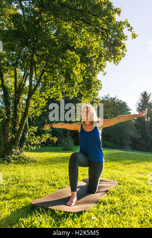 Esercizio di riscaldamento, giovane donna in abbigliamento sportivo facendo allenamento sul tappeto nel parco, Monaco di Baviera, Baviera, Baviera, Germania Foto Stock