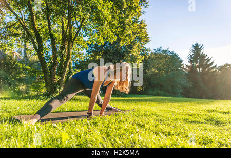 I gruppi laterali, giovane donna in abbigliamento sportivo facendo allenamento sul tappeto nel parco, Monaco di Baviera, Baviera, Baviera, Germania Foto Stock