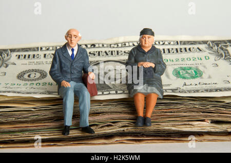 Coppia di anziani, figurine, seduti su una pila di fatture del dollaro, immagine simbolica per eredità Foto Stock