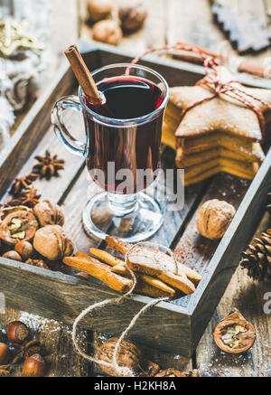 Bicchiere di vino brulé nel vassoio in legno con Natale gingerbread cookies, dadi, cannella, anice e pigne su legno rustico Foto Stock