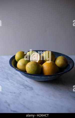 Organici freschi Limoni in una ciotola blu su bianco tavola di marmo Foto Stock