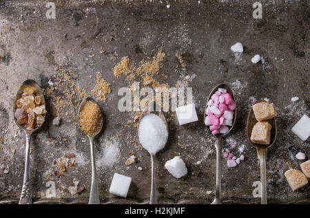 Vintage diversi cucchiai con varietà di zucchero bianco, marrone rosa granulato di frutta, cubi e cristallo su vecchio texture backg ferro Foto Stock