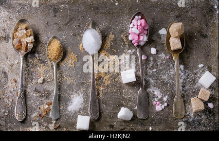 Vintage diversi cucchiai con varietà di zucchero bianco, marrone rosa granulato di frutta, cubi e cristallo su vecchio texture backg ferro Foto Stock