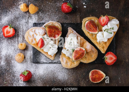 Fette come forma di cuore con giallo lamponi, fragole, a fettine le figure, la ricotta e lo zucchero in polvere in ardesia nera o scheda Foto Stock