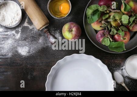 Ingredienti per la produzione di torta di mele. Farina, zucchero, uova rotte in lattine di lattina, mele fresche con foglie in una piastra di metallo, cottura bianco f Foto Stock