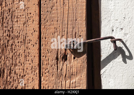 Vecchio arrugginito gancio di chiusura su terreni accidentati porta in legno Foto Stock