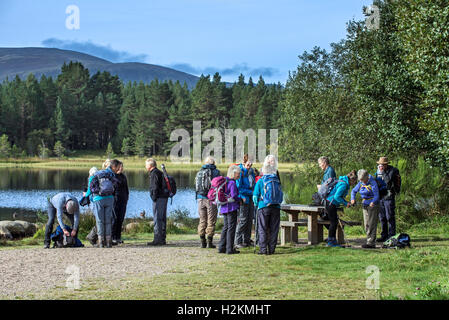 Anziani walkers meeting e preparazione per andare a passeggiare lungo il Loch Morlich in Cairngorm mountains, Highlands scozzesi, Scozia Foto Stock