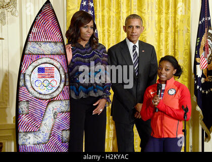 American medaglia d oro-ginnasta vincente Simone Biles, destro presenta un autografo della tavola da surf al Presidente degli Stati Uniti Barack Obama, centro e la first lady Michelle Obama, sinistra, durante una cerimonia di accoglienza il 2016 noi Olimpici e Paralimpici squadre per la Sala Est della Casa Bianca a Washington DC a onorare la loro partecipazione e il successo in questo anno di giochi a Rio de Janeiro in Brasile. Credito: Ron Sachs / Pool via CNP /MediaPunch Foto Stock