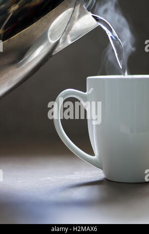 Versando acqua bollente in una tazza di ceramica per creare una bevanda calda. Foto Stock