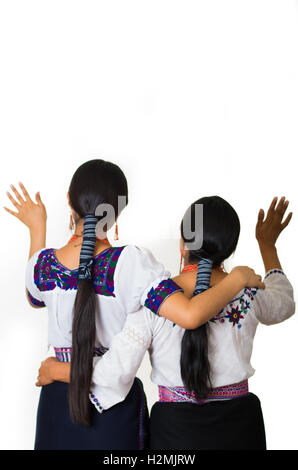 Bella ispanico madre e figlia indossando il tradizionale abbigliamento andina, sia abbracciando mentre sventolano, visto da dietro l'angolo, bianco di sfondo per studio Foto Stock