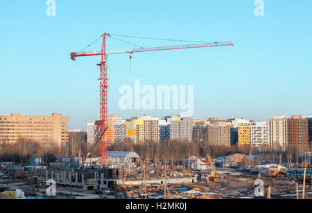 Rosso e bianco edificio gru a torre in corrispondenza di un sito di costruzione contro lo sfondo di edifici moderni. Focus sulla gru Foto Stock