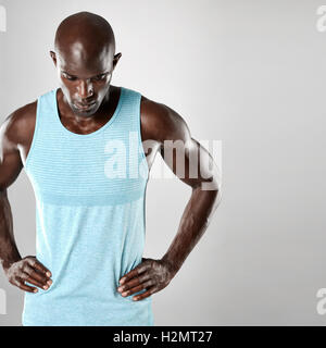 Bel giovane uomo africano con testa calva e bracci muscolare guardando verso il basso su uno sfondo grigio. Foto Stock