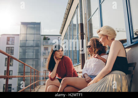 Tre giovani donne seduti all'aperto e chat. Gruppo multirazziale delle femmine rilassarsi in terrazza. Foto Stock