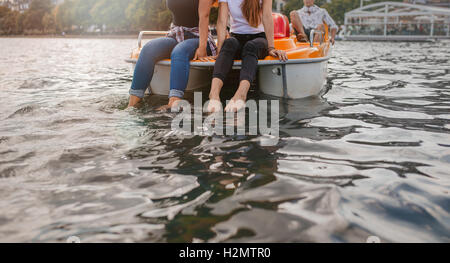 Ritagliato colpo di giovani donne seduta pedale anteriore in barca con i piedi nell'acqua. Due giovani donne su un pedalo. Foto Stock