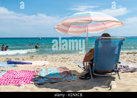 Uomo seduto sotto un ombrellone sulla spiaggia di Le Lavandou area, Regione Provenza-Alpi-Costa Azzurra, Francia Foto Stock