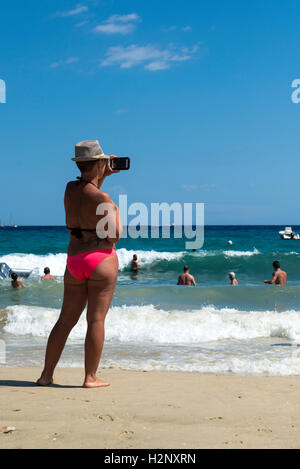 Donna di scattare una foto con uno smartphone sulla spiaggia di Le Lavandou, Regione Provenza-Alpi-Costa Azzurra, Francia Foto Stock
