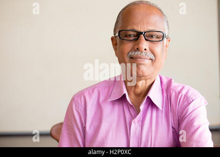 Closeup ritratto, smart anziano Uomo in camicia rosa scuro con occhiali, specifiche, seduti, isolato in interni lavagna bianca Foto Stock