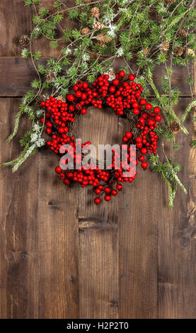 Albero di natale rami e corona da bacche rosse sul legno rustico sfondo. Festosa decorazione della casa Foto Stock