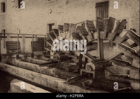 Vecchie ruote di un mulino ad acqua. In stile vintage foto. Aggiunta di grano per dare una vecchia foto effetto. Foto Stock