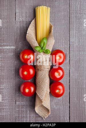 Materie spaghetti in tela di lino con pomodori e basilico sul tavolo di legno Foto Stock