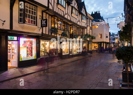 In una buia sera d'inverno, gli acquirenti di Natale passano da una sfocatura di movimento - una festosa, illuminato Stonegate, York, Inghilterra. Foto Stock