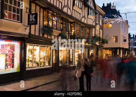 In una buia sera d'inverno, gli acquirenti di Natale passano da una sfocatura di movimento - una festosa, illuminato Stonegate, York, Inghilterra. Foto Stock