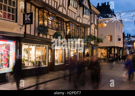 In una buia sera d'inverno, gli acquirenti di Natale passano da una sfocatura di movimento - una festosa, illuminato Stonegate, York, Inghilterra. Foto Stock