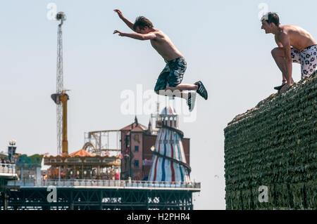 Gli adolescenti che salta da pennelli sulla spiaggia di Brighton nel mare in un pomeriggio caldo. Foto Stock