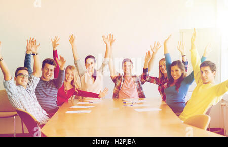 Gruppo di studenti sorridente alzando le mani in office Foto Stock