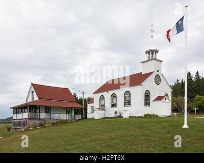 L'Acadian sventola davanti alla cappella di Sant'Anna de Beaumont e il presbiterio che sono state costruite in1842. Foto Stock